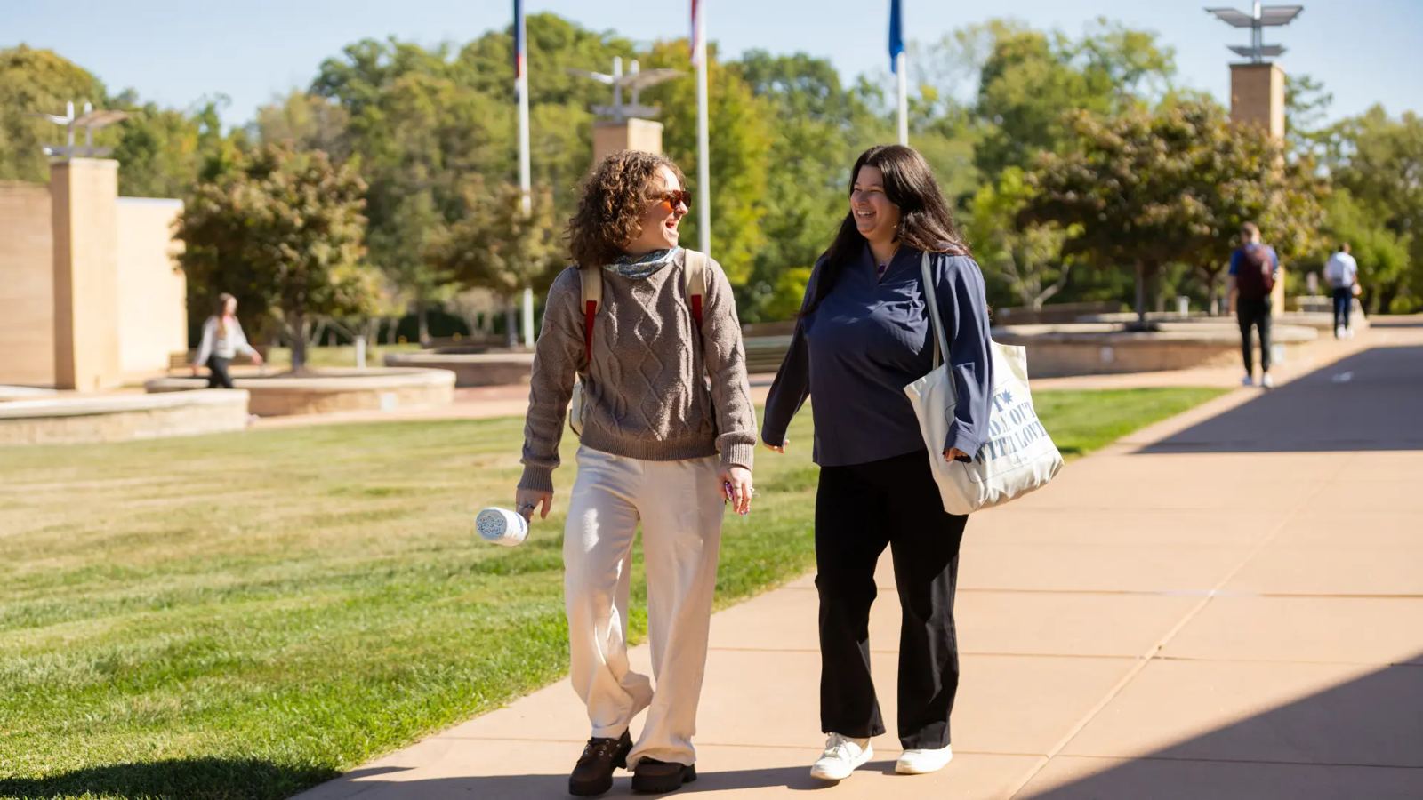 Two Logan University students laughing as they walk along a sunny campus path