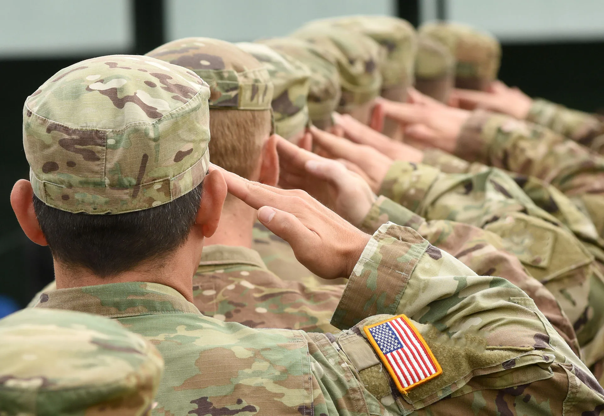 Service members in camouflage uniforms saluting