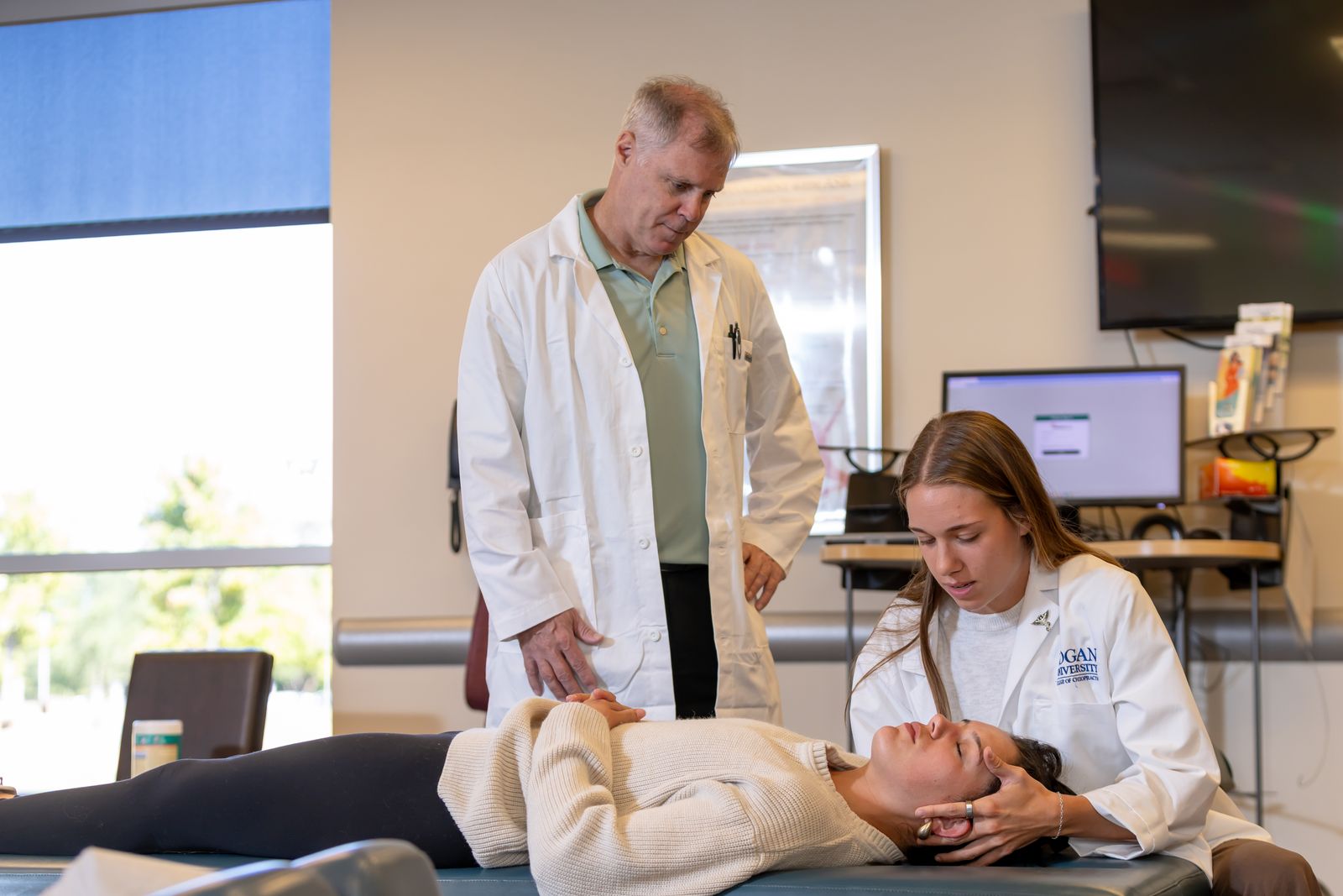 A supervising clinician looks on as a Logan student clinician works with a patient