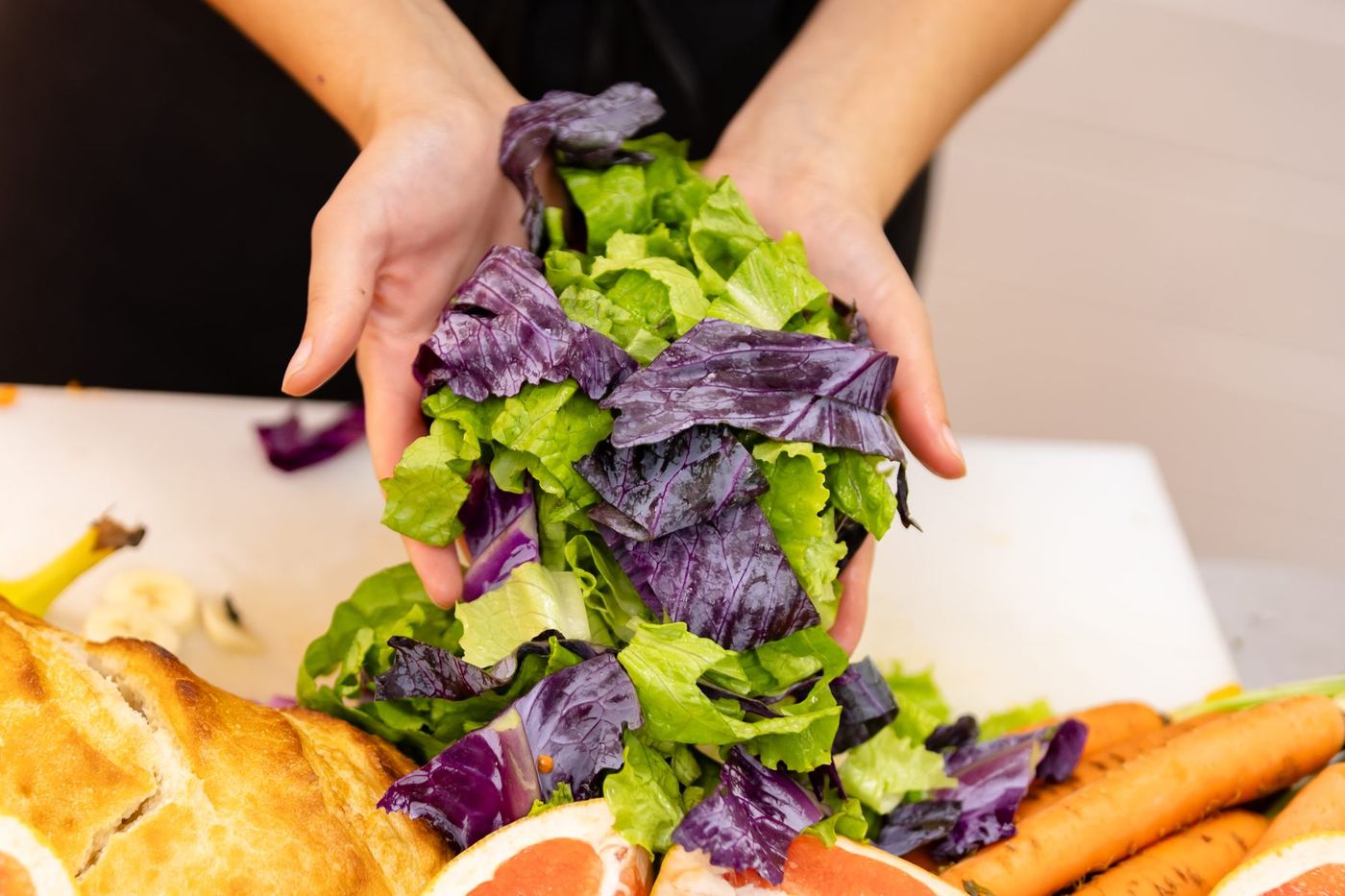 Hands hold fresh green and purple lettuce above a cutting board with various fruits and vegetables.