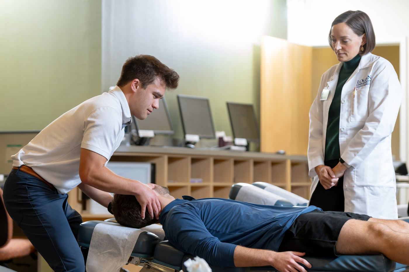 Logan University student performs a neck adjustment on a patient, instructor observes in a clinical setting.