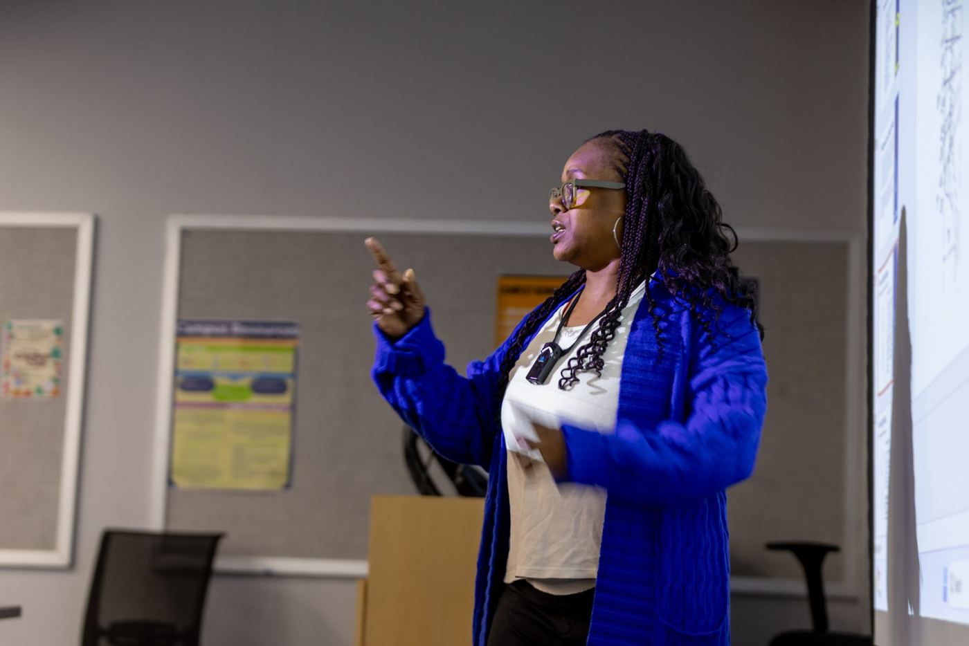 Woman with braided hair and glasses, wearing a blue cardigan, presents at Logan University.
