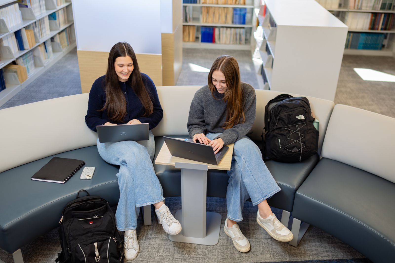 Two students work on laptops in a Logan library lounge