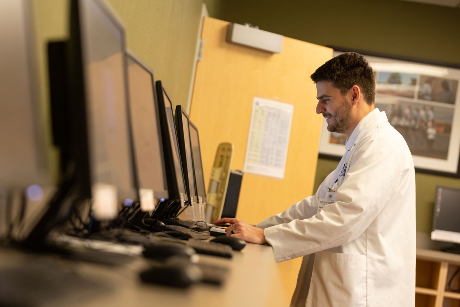 A clinician in a white coat works at a bank of computer monitors