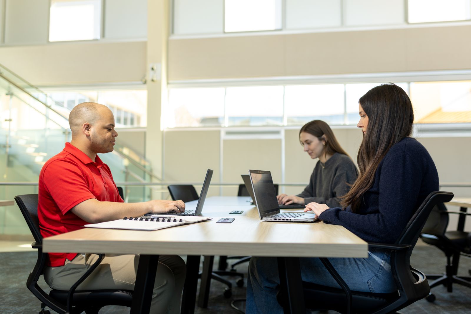 Students work on laptops at a table in a bright Logan study space