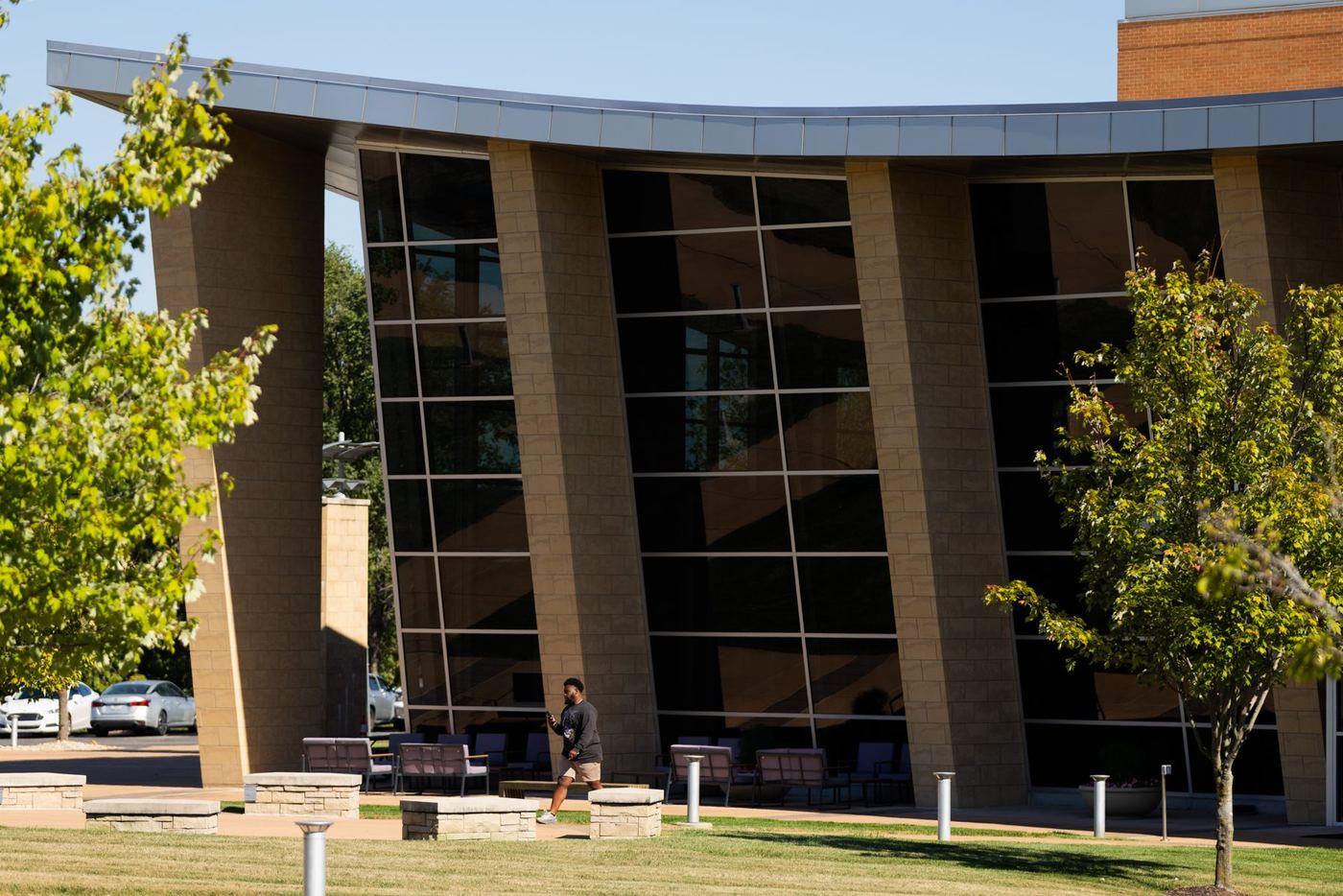 Man walks on a sunny campus lawn in front of a modern building with large reflective windows at Logan University.
