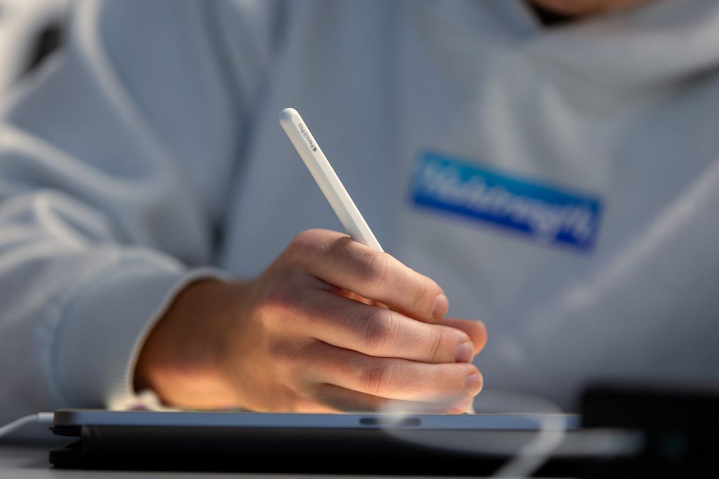 Close-up of a hand holding an Apple Pencil Pro, drawing or writing on a tablet screen.