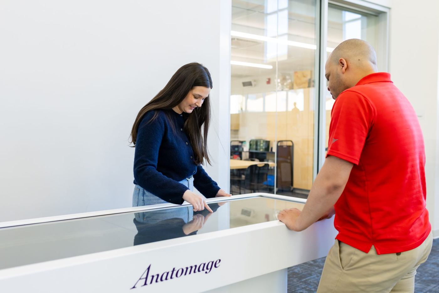 Female student and male faculty interact with a large Anatomage table in a modern university lab.