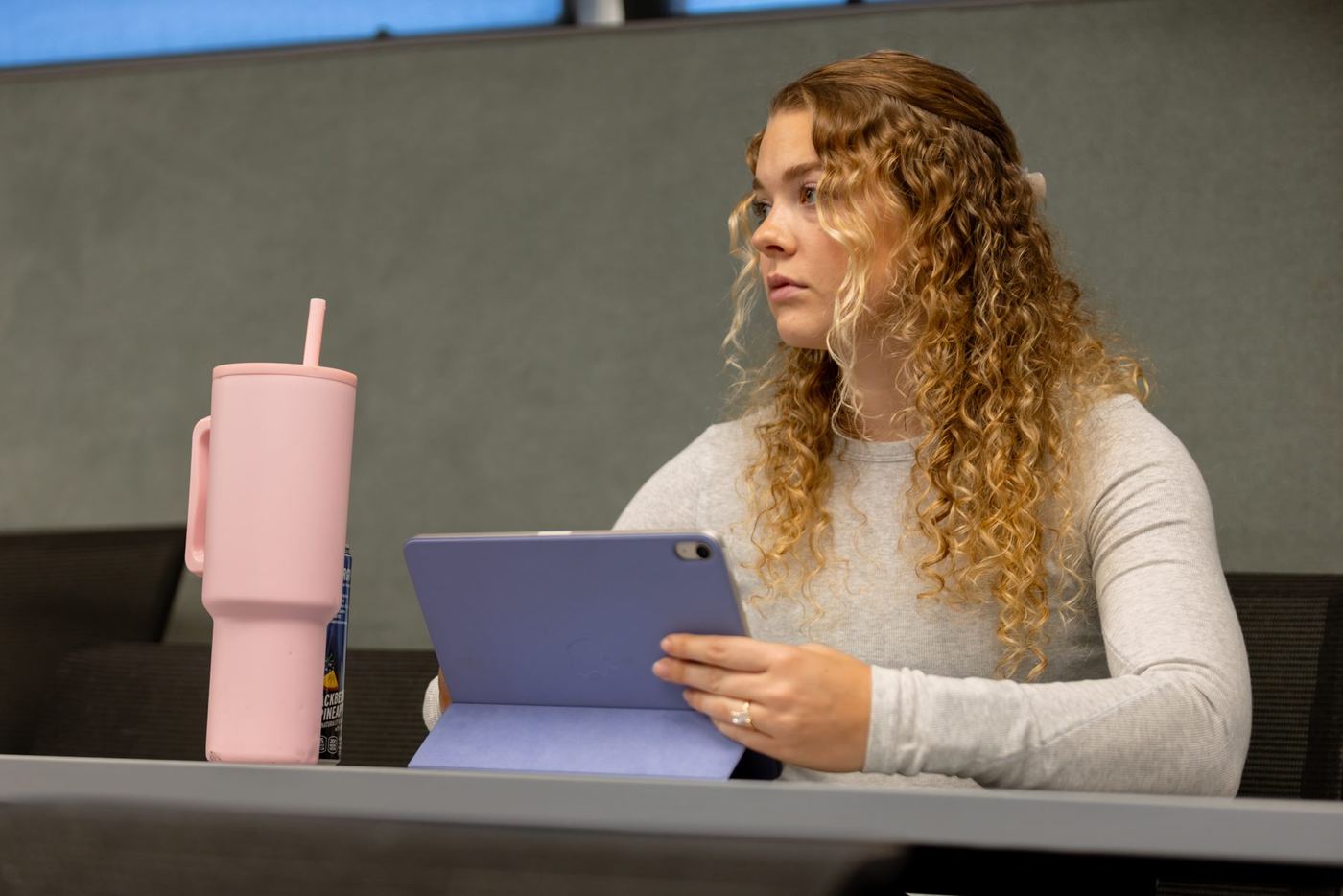 Young woman with curly blonde hair looks intently at a purple tablet at a desk.