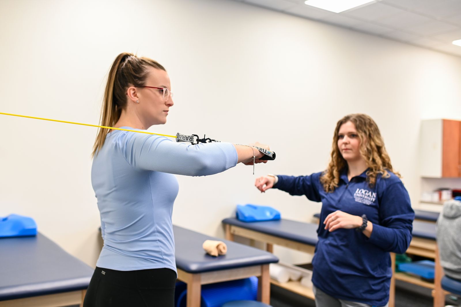 A student works through a resistance-band exercise while a Logan instructor coaches
