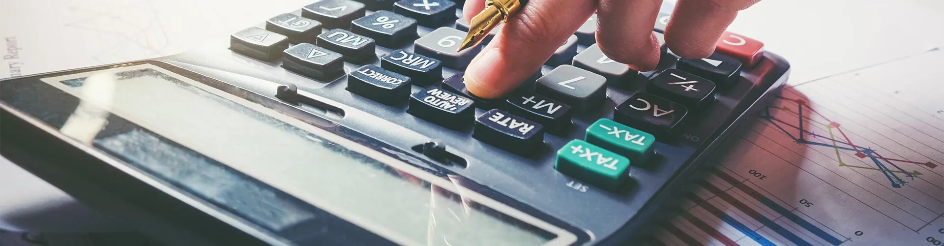 Hand using a calculator beside a financial chart