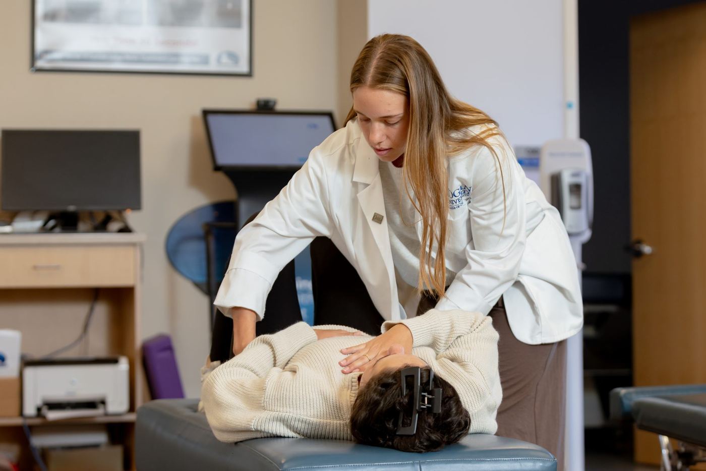 Logan University student in lab coat performs a chiropractic adjustment on a patient.