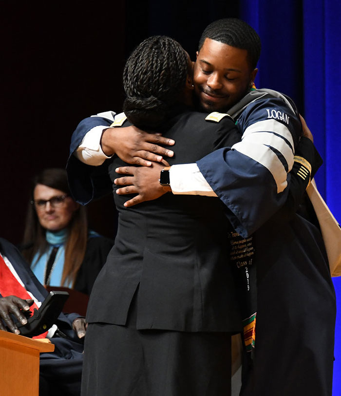 Male student hugging teacher at graduation.