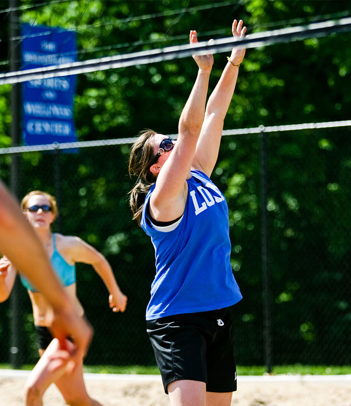 Female student playing sand volleyball on campus.
