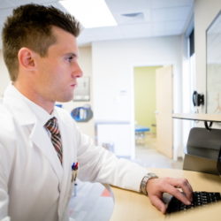 A male health center clinician consults with a patient via telehealth on a desktop computer