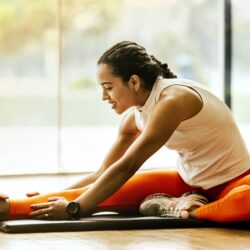 Women in white tank top and orange leggings stretches on the ground