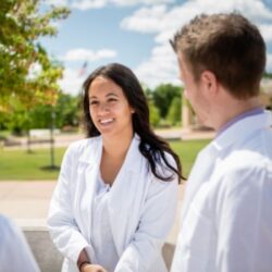 Three students stand in a circle talking on Logan University's campus