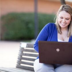 A woman sits on a bench with a laptop